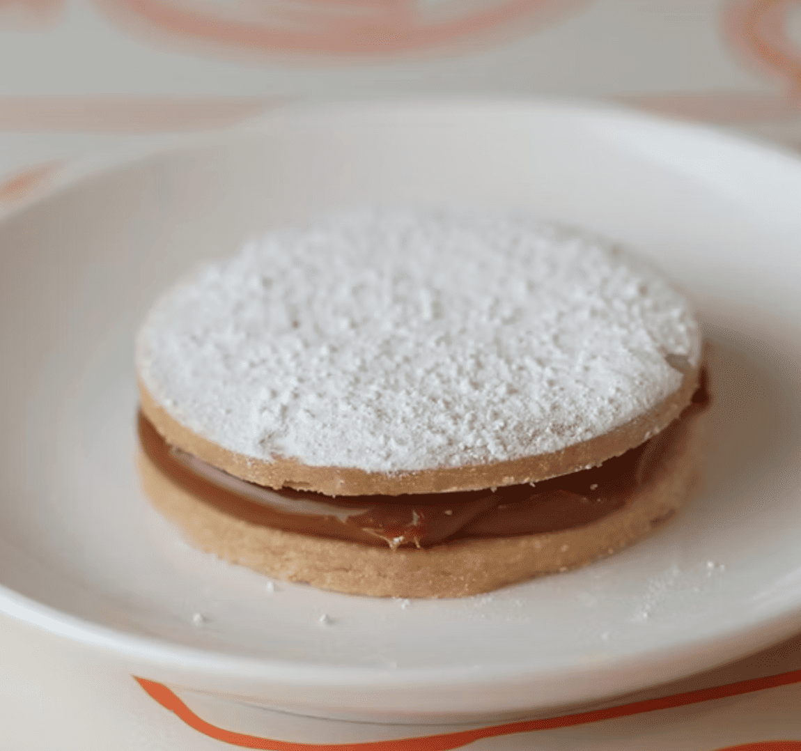 Alfajor relleno de dulce de leche, espolvoreado con azúcar glas.