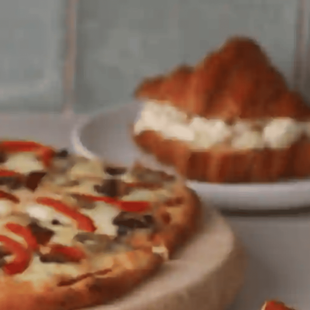 Pizza con rodajas de tomate fresco, queso derretido y pesto sobre salsa de tomate.