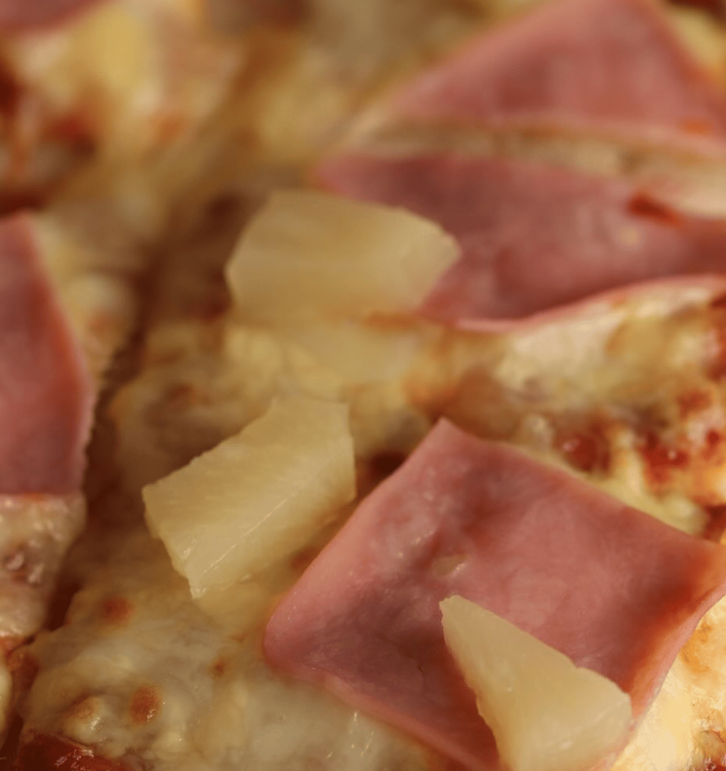 Pizza con jamón, queso fundido y trozos de piña sobre salsa de tomate.